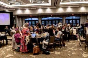 The Sandtray Summit ballroom with round tables, arched windows and ring chandeliers