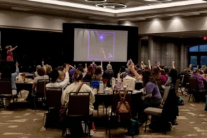 The Sandtray Summit ballroom from the back, dozens of hands raised during a session