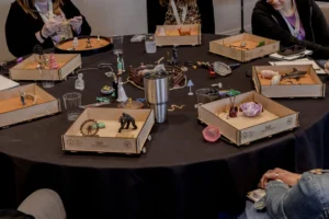A round table of small wooden IAST sandtrays mid-exercise at the Sandtray Summit