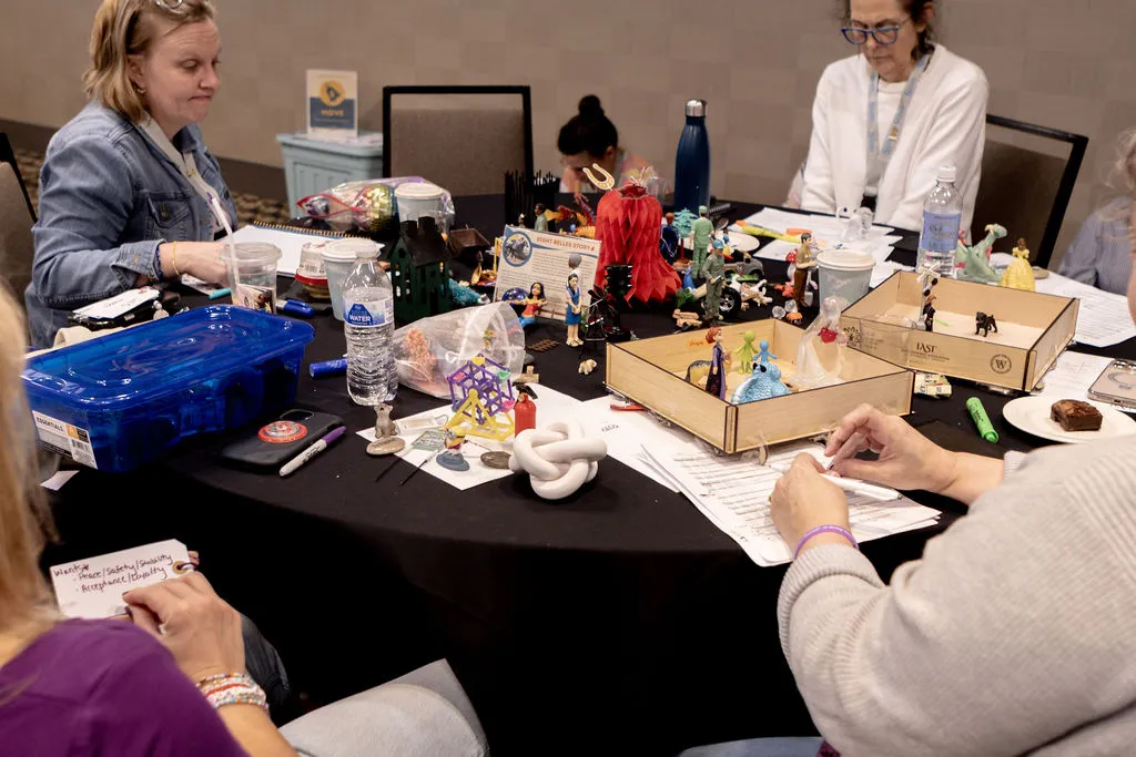 Therapists around a table building small sandtrays and taking notes beside bins of miniatures